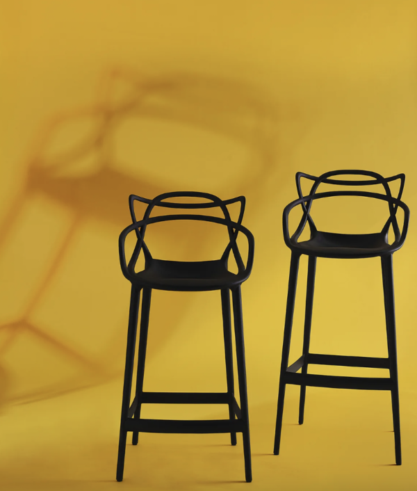 Kartell Bar Height and Counter Height Stools in black photographed against a yellow backdrop.